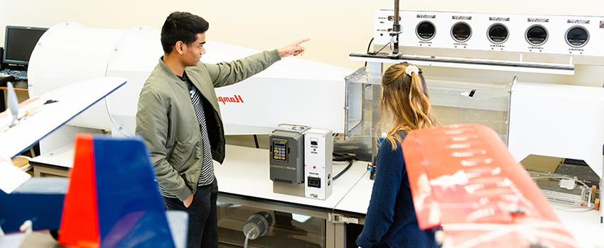 Male student pointing to a machine in mechanical lab.